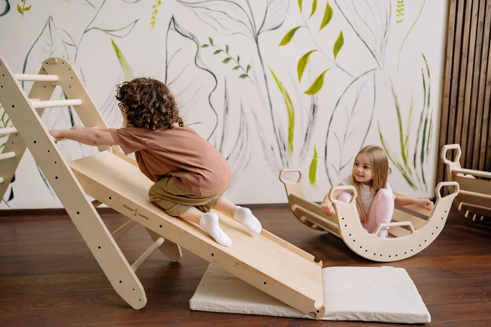 Children play on indoor wooden climbing and rocking equipment; illustrative marketing photograph.
